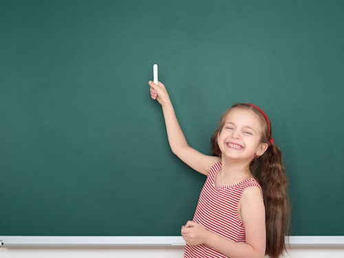 schoolgirl child in red striped dress point and drawing on green chalkboard background, summer school vacation concept
