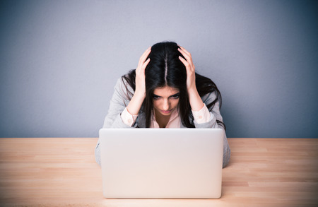 38305673 - tired businesswoman sitting at the table over gray background. looking on laptop
