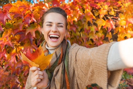 45387366 - portrait of cheerful young woman with autumn leafs in front of foliage making selfie