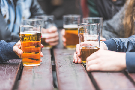 45837435 - hands holding glasses with beer on a table at pub in london. a group of friends is enjoying beer time in the city, close up on the glasses.